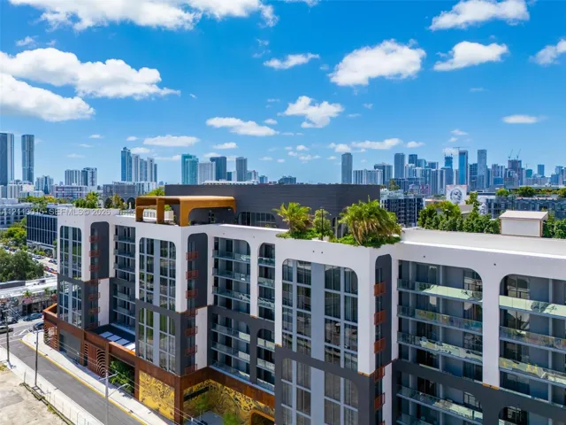 Modern multi-story building facade featuring arched architectural details, private glass-railed balconies, a rooftop terrace with mature landscaping, and multi-toned exterior paneling