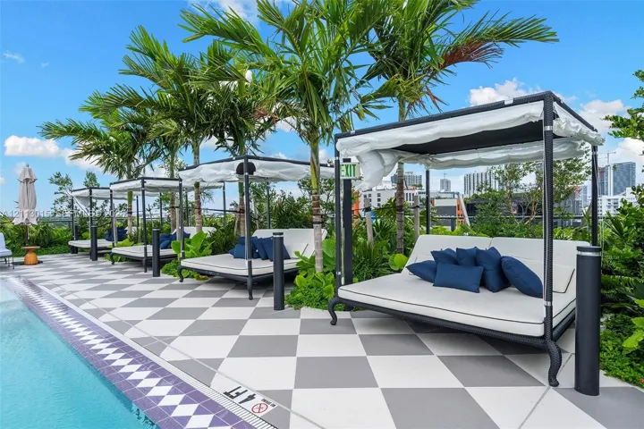 Rooftop pool deck featuring a geometric tiled surface, built-in poolside lounge structures, mature palm trees, and perimeter metal railing