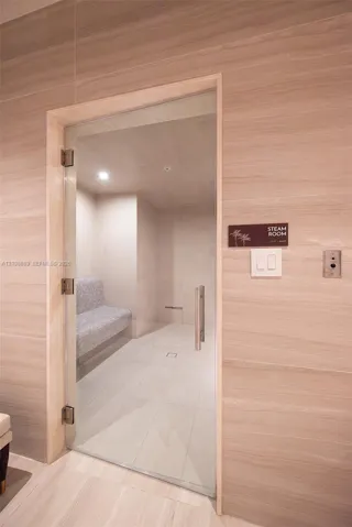 Steam room featuring a frameless glass door, floor-to-ceiling horizontal-grain stone wall cladding, recessed ceiling lighting, and a built-in tiled bench