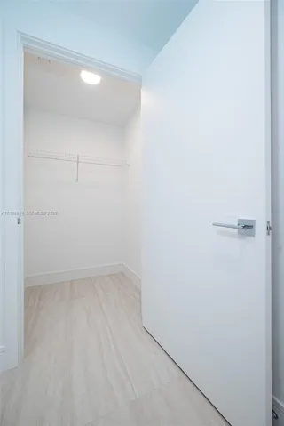 Walk-in storage space featuring wood-finish flooring, a white flat-panel door with a square-back plate lever handle, and a mounted wire shelving system