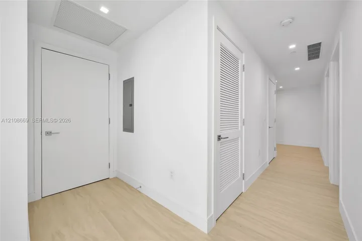 Hallway featuring light-toned wood-finish flooring, recessed ceiling lighting, and crisp white walls