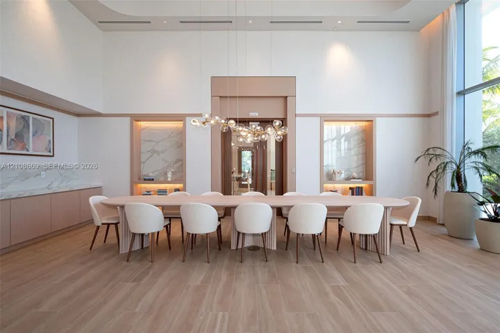 Double-height ceilings featuring recessed lighting, floor-to-ceiling windows, light wood-finish flooring, custom built-in cabinetry with stone slab accents, and a sculptural multi-globe pendant light fixture