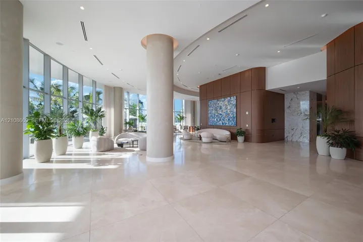 Expansive lobby featuring floor-to-ceiling glass walls, large-format tile flooring, wood-paneled walls, and structural columns with recessed lighting