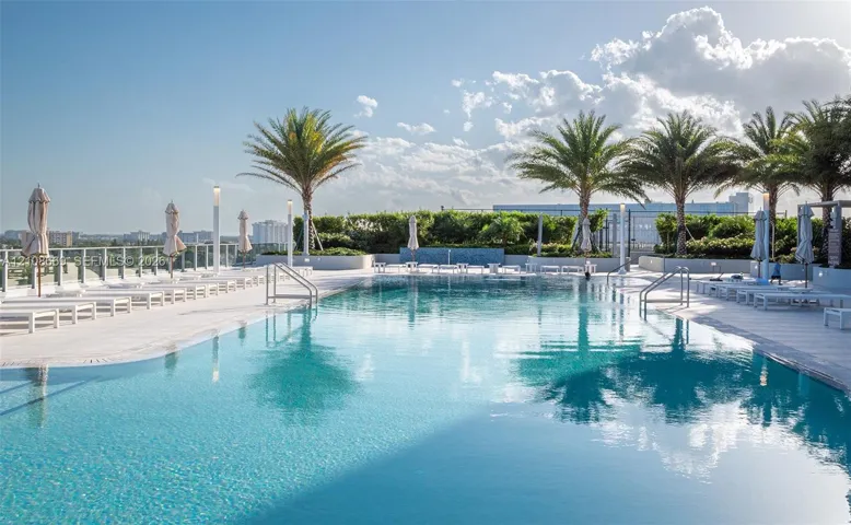 Rooftop swimming pool featuring a tiled deck, metal railings, integrated lighting, and palm tree landscaping