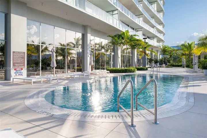 Swimming pool with stainless steel railings, light-colored tile decking, and floor-to-ceiling exterior glazing