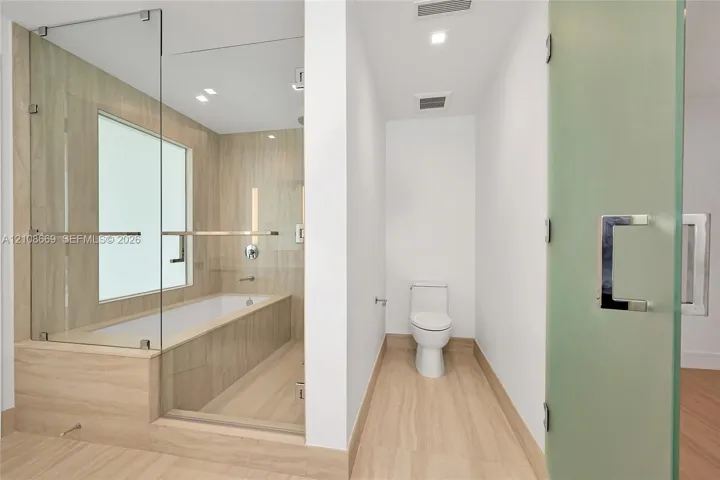 Glass-enclosed soaking tub, tile surround, recessed lighting, and frosted glass door