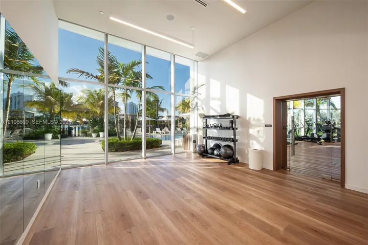 Floor-to-ceiling windows, wood-finish flooring, full-wall mirrored paneling, and high ceilings with integrated linear lighting