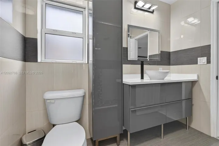 Modern floating vanity featuring a glossy grey finish, white countertop, vessel sink, and matte black faucet, complemented by full-height wall tiling with contrasting horizontal banding