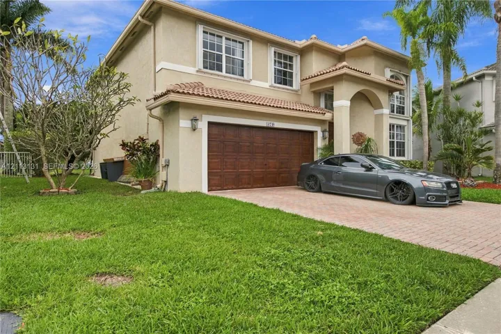 Stucco exterior featuring a dual-pitch tile roof, paver driveway, and a wood-finish two-car garage door