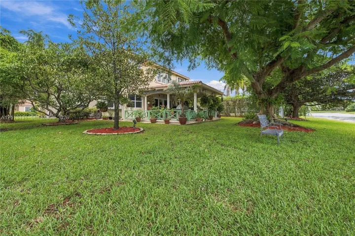 Expansive backyard featuring a sprawling lawn, mature trees, tiered landscape beds with mulch, and a covered patio area with railing