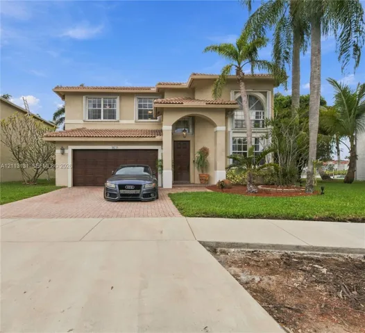 Two-story stucco exterior featuring a clay tile roof, arched entryway, multi-paned windows, and a paver driveway