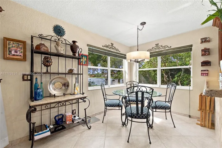 Corner dining area featuring large windows with exterior water scenery, neutral tile flooring, and an overhead drum-style pendant light fixture