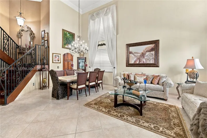 Two-story ceiling height, wrought iron staircase railing, multi-light crystal chandelier, oversized arched window, and ceramic tile flooring