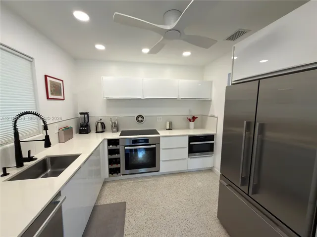 Modern kitchen featuring flat-panel white cabinetry, stone-finish countertops, stainless steel appliances, a built-in wine rack, and terrazzo flooring