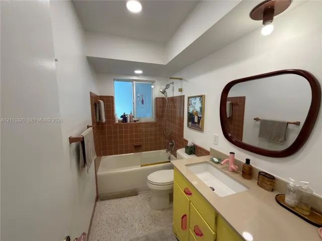 Bathroom featuring a vanity with integrated rectangular sink, solid surface countertop, tiled tub surround, recessed lighting, and terrazzo-style flooring