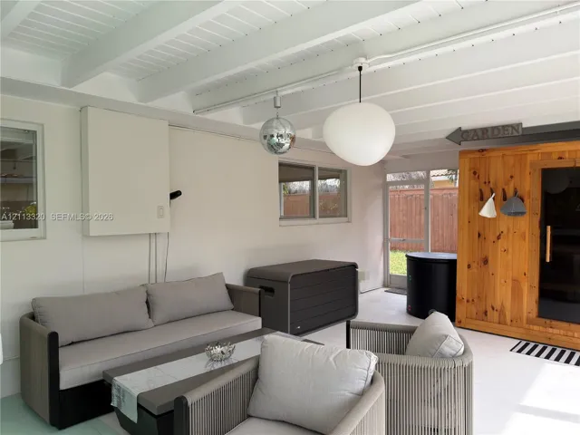 Covered patio featuring an exposed-beam ceiling, glass-paneled exterior door, pendant lighting, and a built-in wooden structure