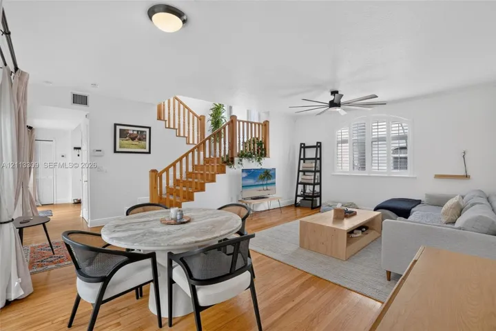 Open floor plan featuring wood-finish flooring, a central staircase with wood railings, and a multi-pane arched window with plantation shutters