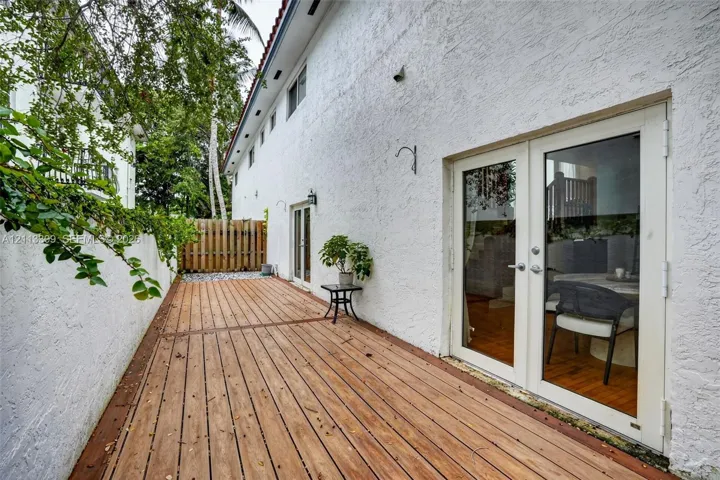 Exterior wood-finish decking featuring dual glass-paned double doors, white textured stucco walls, and a perimeter wood fence
