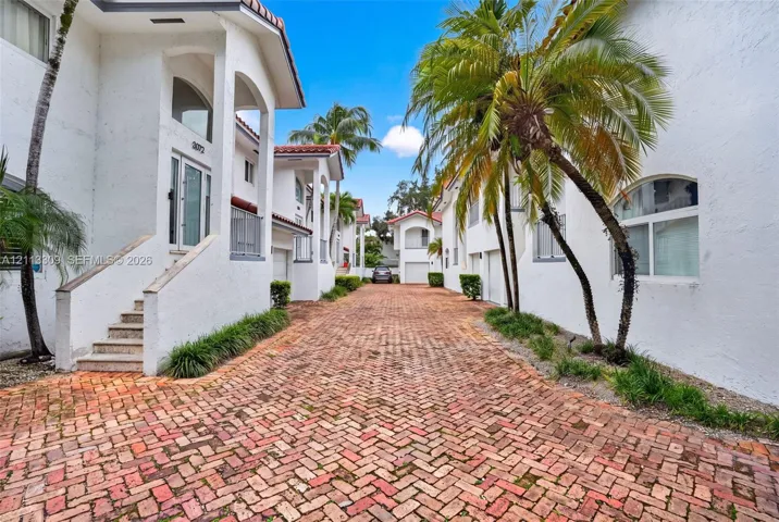 Stucco exterior featuring arched architectural detailing, a herringbone-patterned brick paver motor court, and mature palm landscaping
