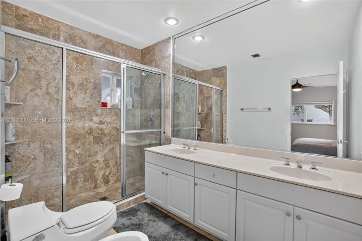 Dual-sink vanity with a solid-surface countertop, floor-to-ceiling framed mirror, and a walk-in shower featuring tile surrounds and a glass enclosure