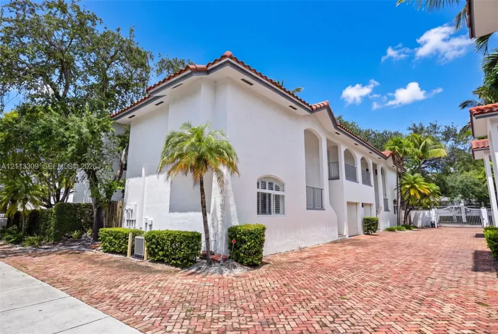 Stucco exterior featuring arched architectural detailing, a clay tile roof, second-story balconies, and a red brick driveway