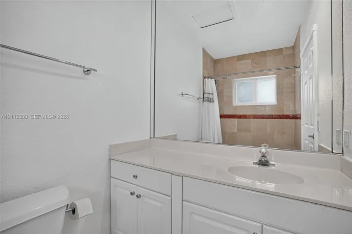 Bathroom featuring a white vanity with a solid surface countertop, an integrated sink, a full-width vanity mirror, and a tub-shower combination with tile surround