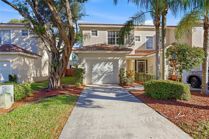 Stucco exterior with a tiled roof, attached garage, concrete driveway, and established landscaping
