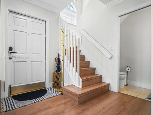Foyer featuring wood-finish flooring, a staircase with wood-finish treads and white balusters, crown molding, and a vaulted arched window