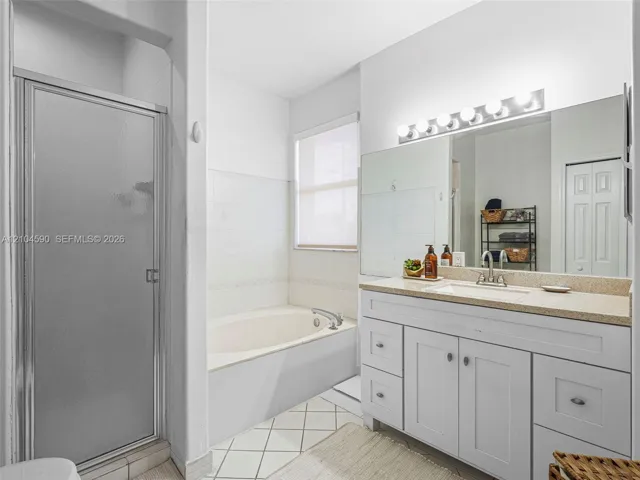 Bathroom featuring a white vanity with integrated basin, light-toned countertop, large wall-mounted mirror, separate soaking tub, and a glass-enclosed shower