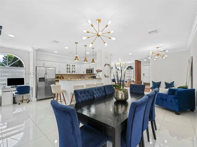 Open-concept area featuring polished tile flooring, contemporary multi-arm chandeliers, white cabinetry with integrated appliances, and an arched window