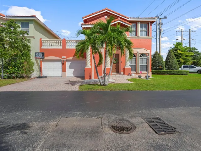 Two-story Mediterranean-style exterior featuring a tile roof, decorative columns at the entrance, a second-story balcony with balustrade railing, and a paved driveway