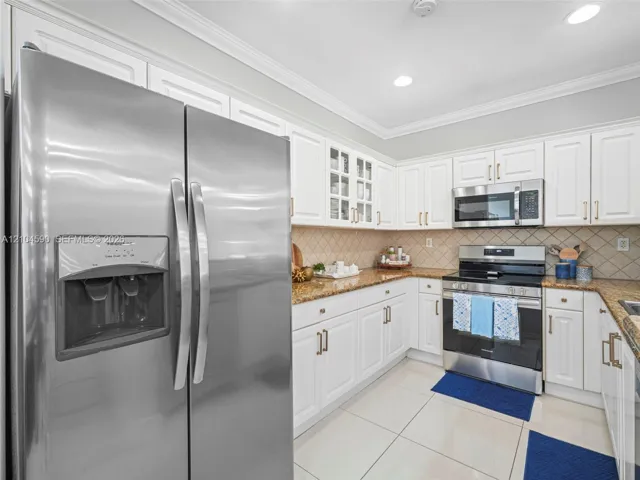 Kitchen featuring white cabinetry, stone countertops, stainless steel appliances, glass-front upper cabinet doors, and tile flooring