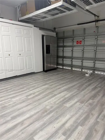 Garage area featuring wood-finish flooring, built-in white dual-panel closet doors, stainless steel refrigerator, and overhead wire storage shelving