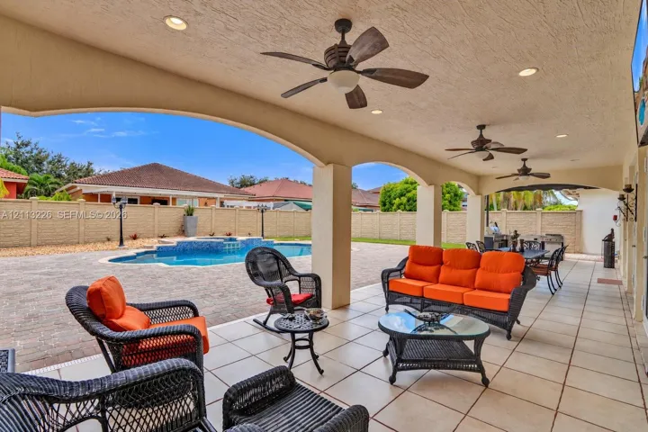 Covered lanai featuring a tile floor, arched structural supports, recessed lighting, and ceiling fans, with an outdoor pool and paved patio area
