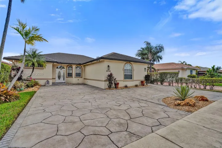 Single-story stucco exterior featuring a tiled roof, decorative arched windows, a patterned paver driveway, and mature landscaping