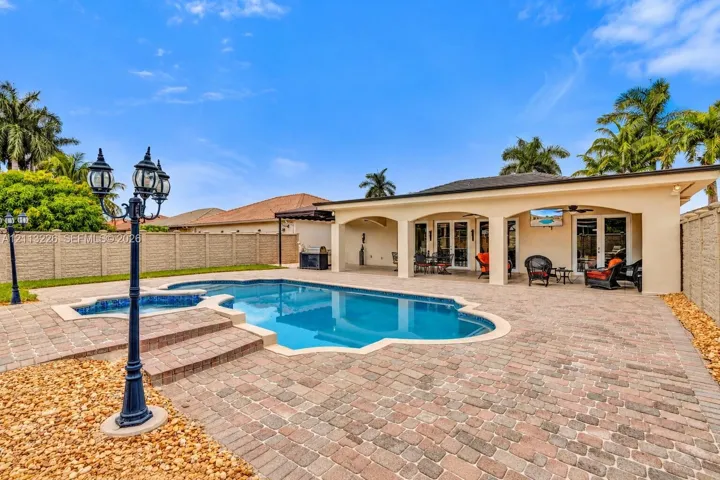 Outdoor area featuring a swimming pool with integrated spa, paver patio, covered loggia with arched architecture, and decorative post lighting, enclosed by a perimeter wall