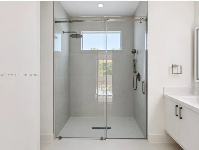 Walk-in shower featuring large-format tile surround, frameless glass sliding enclosure, rainfall showerhead, handheld sprayer, and transom window