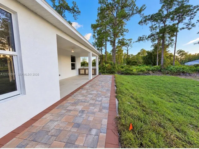 Covered patio featuring a multi-tone paver floor, built-in outdoor cabinetry, and a ceiling fan, bordered by a manicured lawn