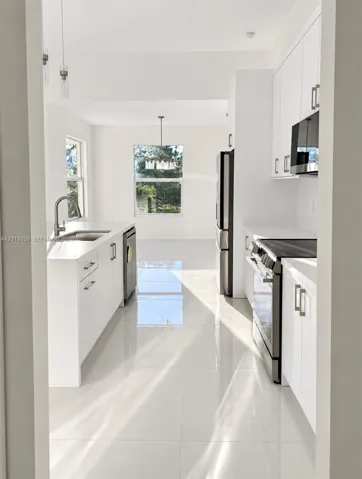 Kitchen featuring white cabinetry, solid-surface countertops, large-format tile flooring, stainless steel appliances, and a polished chrome kitchen faucet