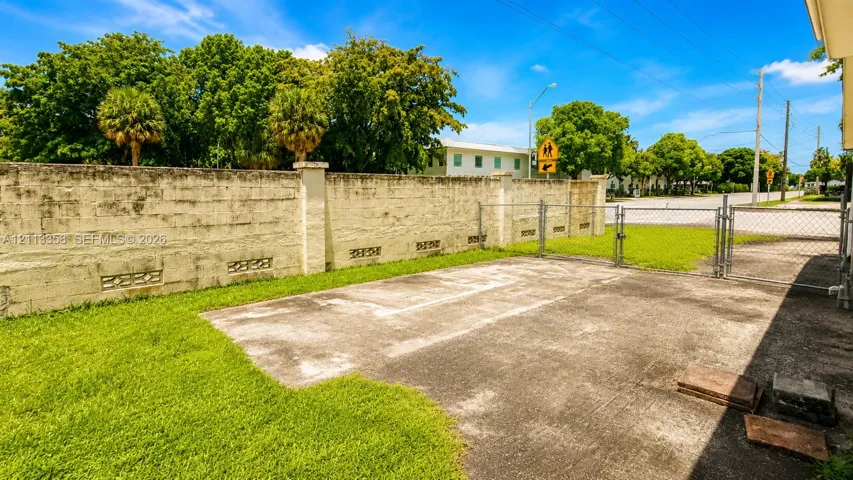 Concrete parking pad featuring a perimeter masonry wall and a chain-link gate
