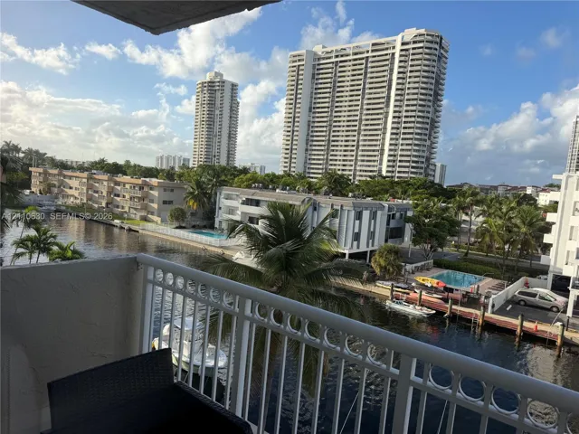 Private balcony with white metal railings overlooking a canal, watercraft, and dense palm tree foliage