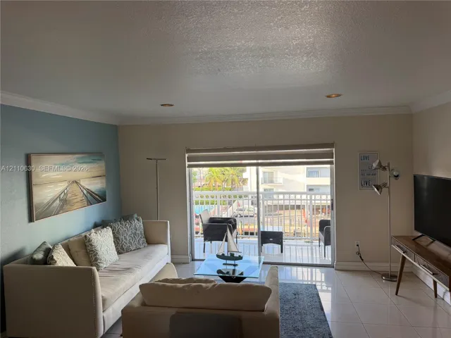 Living space featuring large-format tile flooring, crown molding, recessed lighting, and a sliding glass door providing access to a private balcony