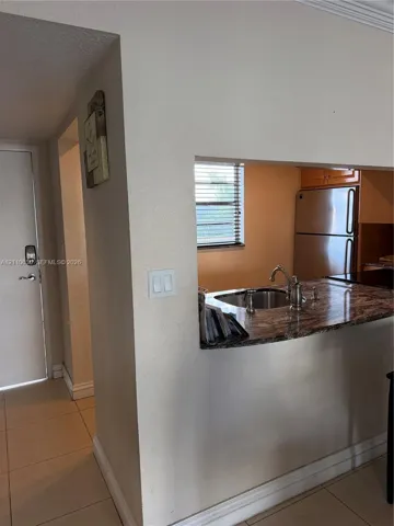 Kitchen pass-through featuring a stone-surface countertop, stainless steel sink with a high-arch faucet, and tile flooring