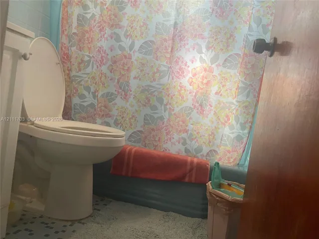 Bathroom featuring a standard toilet, a tub with a solid-color surround, and tiled flooring