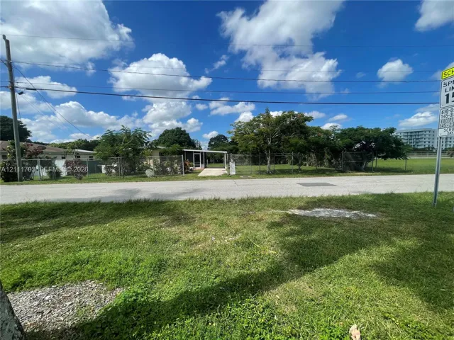 Single-story residence featuring a covered entryway, paved driveway, and chain-link fencing enclosing the property grounds