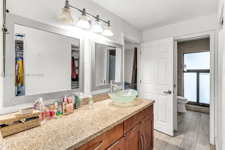 Bathroom vanity featuring a speckled stone-finish countertop, dual wood-tone cabinets, glass vessel sink, and large framed wall​​‌​​​​‌​​‌‌​‌‌​​​‌‌​‌​‌​‌​​​‌​​ mirrors