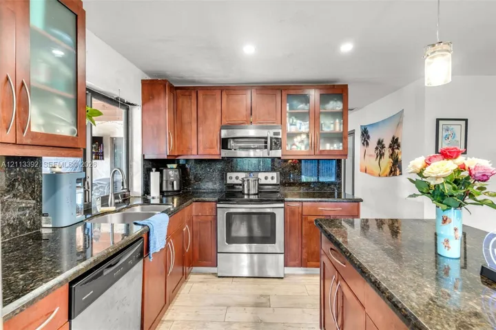 Kitchen featuring custom wood cabinetry, dark stone countertops, stainless steel appliances, glass-front upper cabinets, and wood-finish flooring