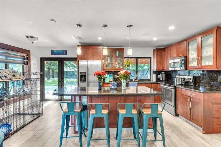 Kitchen featuring wood cabinetry, stone countertops, a center island with pendant lighting, stainless steel appliances, and wood-finish flooring