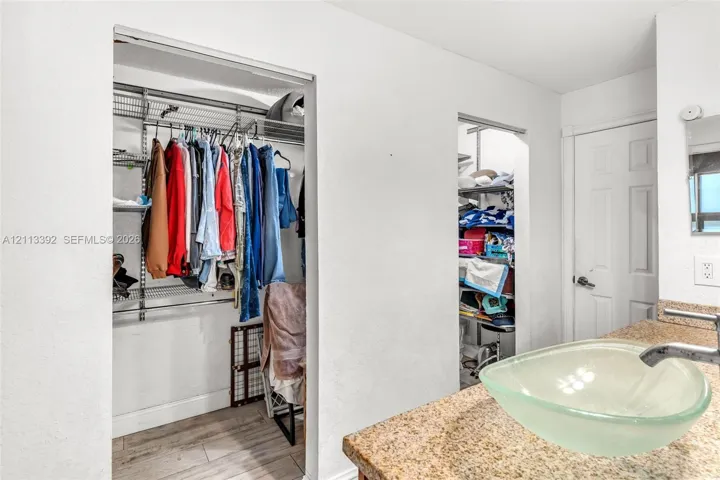 Vanity featuring a stone countertop, glass vessel sink, and chrome faucet, accompanied by walk-in closets with integrated wire shelving and wood-finish flooring