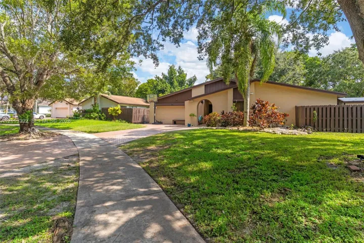 Single-story residence featuring a stucco exterior, arched entryway, paved driveway, mature landscaping, and a fenced side yard